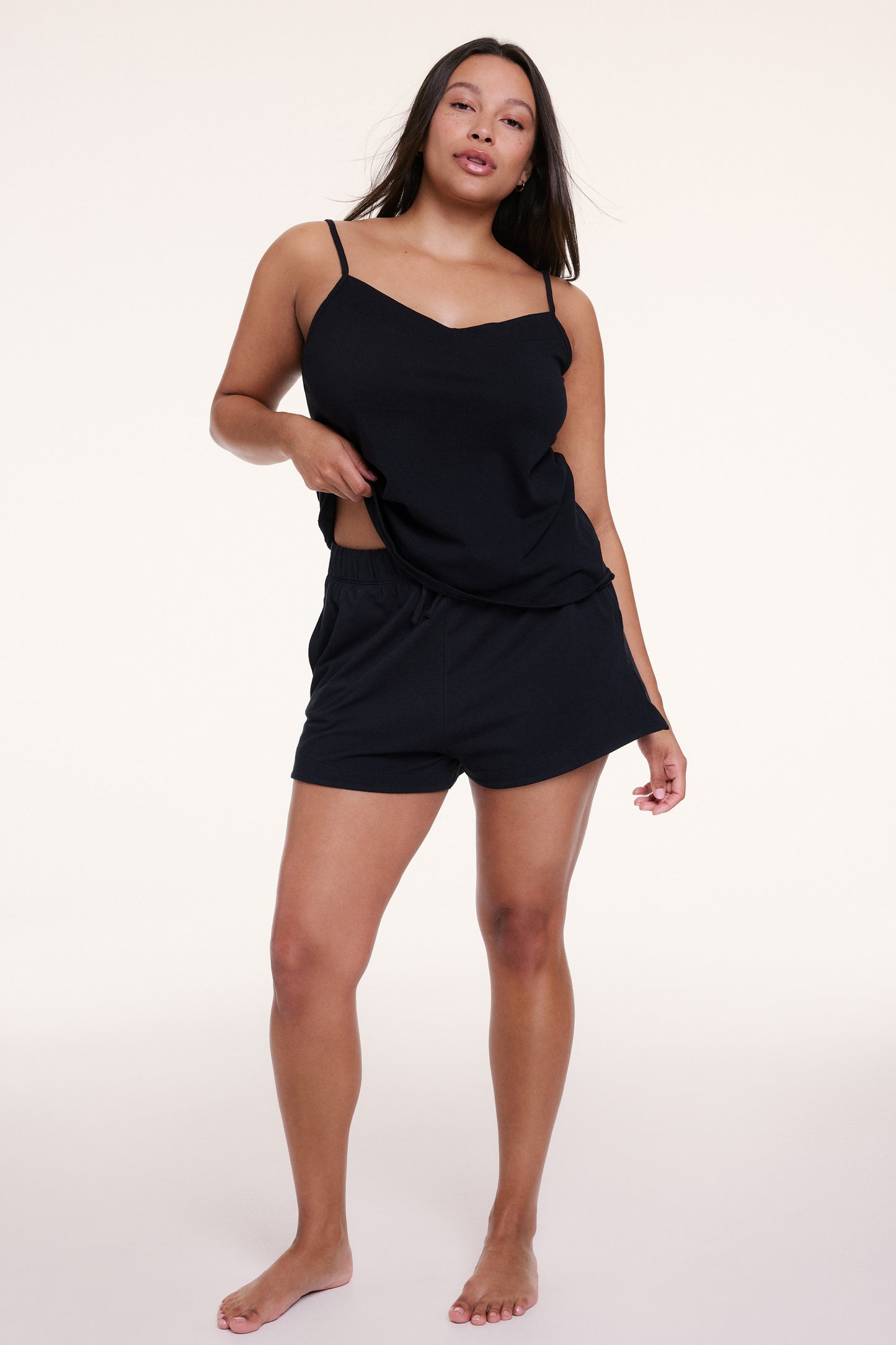 On a white studio backdrop, Alana wears the Sunday Pima Short in Black with a matching tank, featuring a relaxed silhouette, elastic waistband, and adjustable drawstring for all-day comfort.