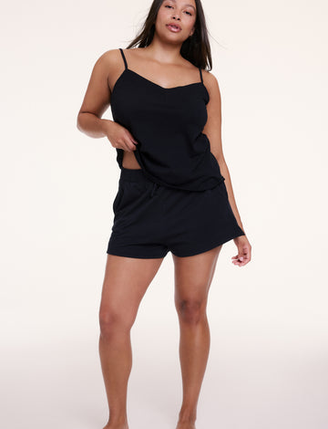 On a white studio backdrop, Alana wears the Sunday Pima Short in Black with a matching tank, featuring a relaxed silhouette, elastic waistband, and adjustable drawstring for all-day comfort.