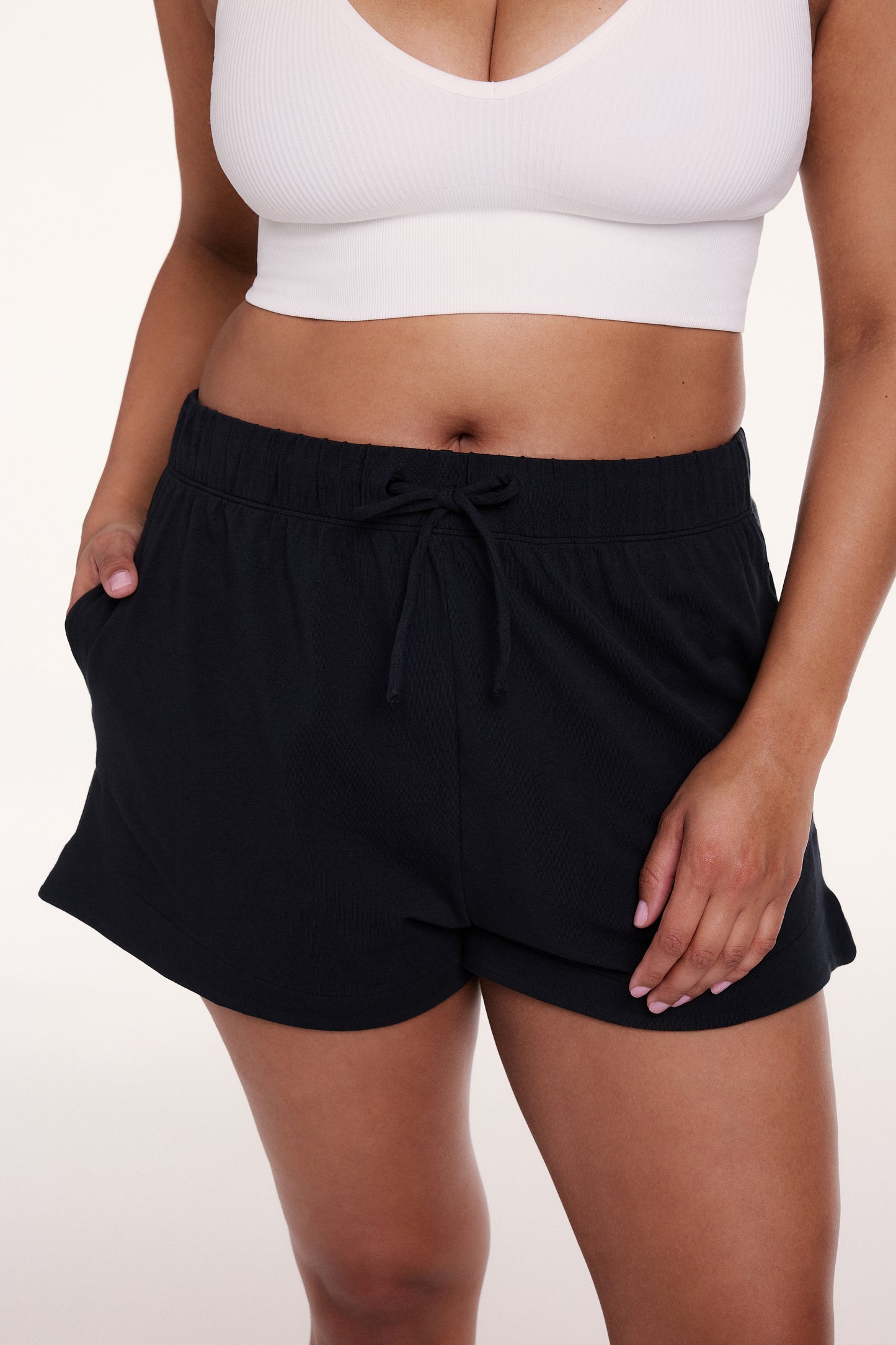 On a white studio backdrop, Alana wears the Sunday Pima Short in Black, focusing on the soft fabric, relaxed fit, and elastic waistband with adjustable drawstring.