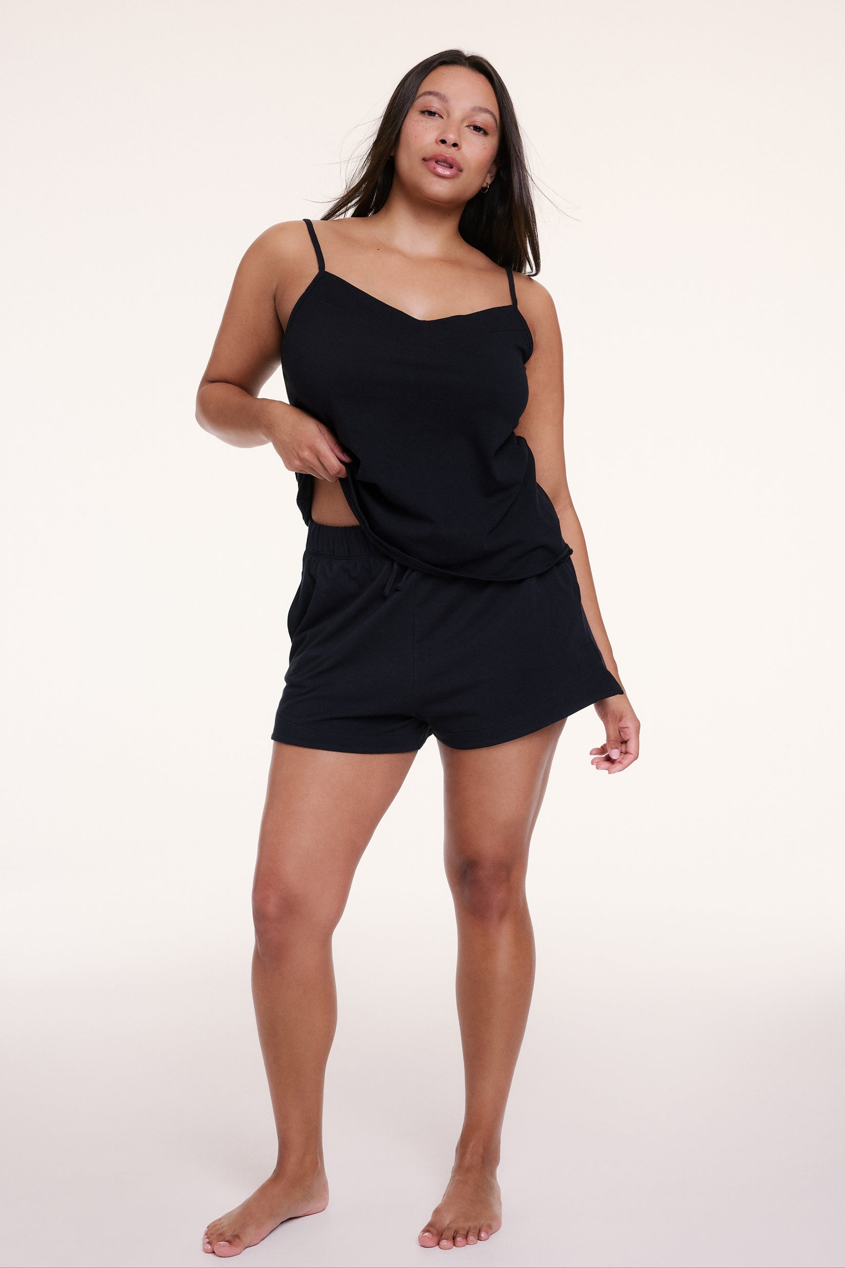 In a studio setting, Alana wears the Sunday Pima Tank in Black with matching shorts, showing the relaxed fit and lightweight, drapey fabric.