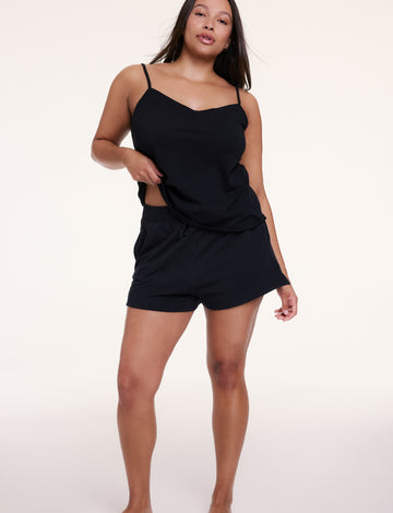 In a studio setting, Alana wears the Sunday Pima Tank in Black with matching shorts, showing the relaxed fit and lightweight, drapey fabric.