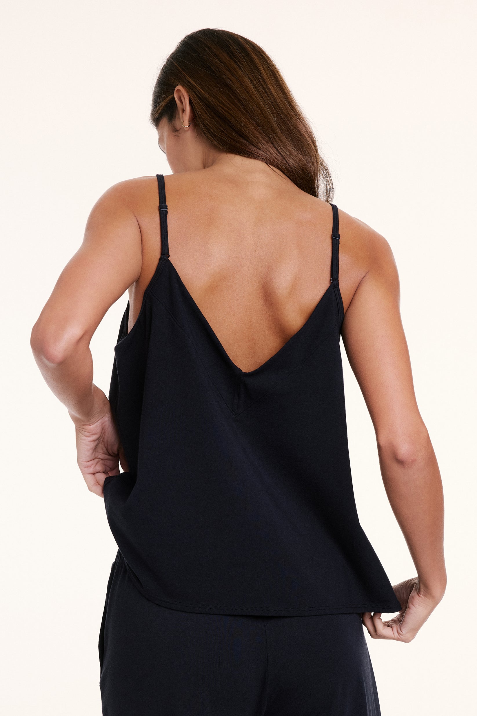 In a studio setting, Linni wears the Sunday Pima Tank in Black, showing the V back, adjustable straps, and relaxed silhouette.