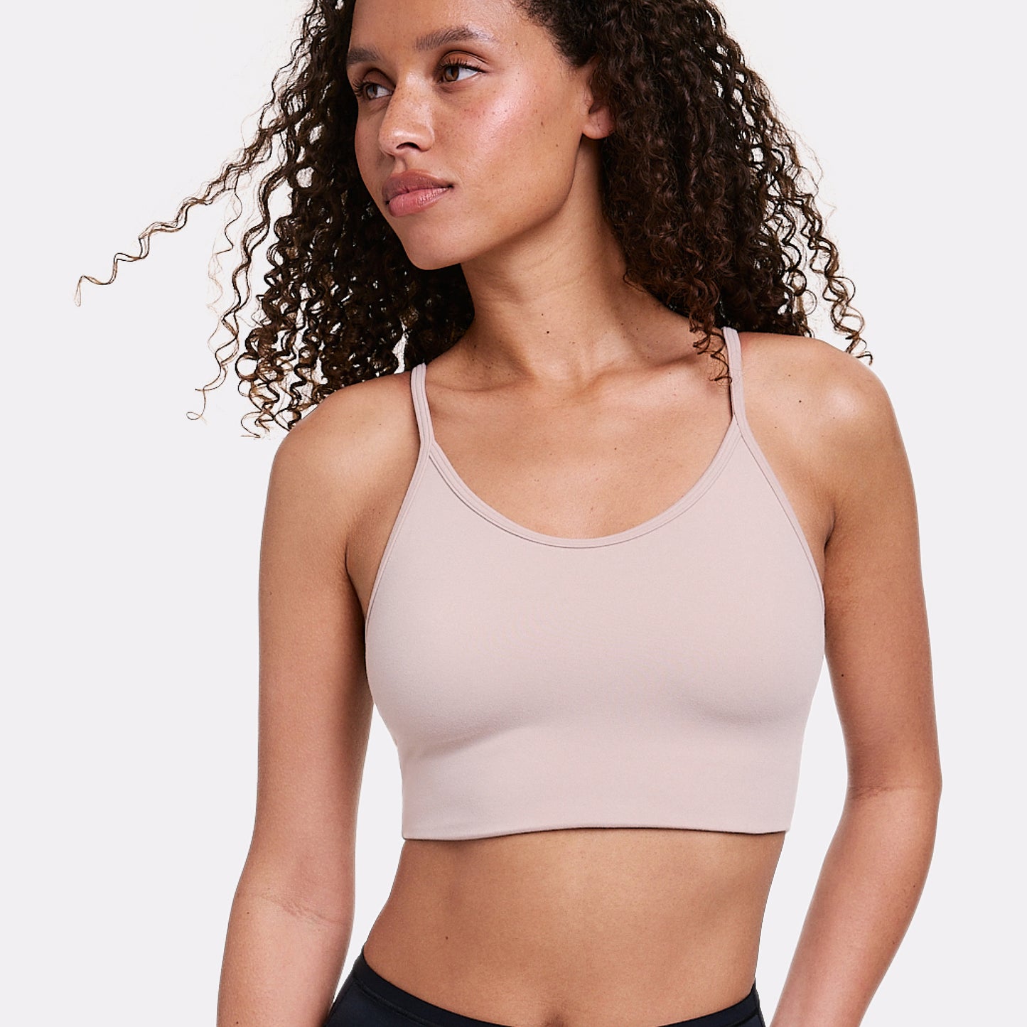 In a light gray studio, Courtney wears the Whipped Knit Scoop Bralette in Mushroom, shown from the waist up with a scoop neckline, thin adjustable straps, and soft, smoothing fabric for comfortable support.
