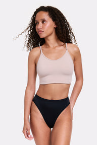 In a light gray studio, Courtney wears the Whipped Knit Scoop Bralette in Mushroom with black underwear, shown in a full-body front view highlighting the scoop neckline, thin adjustable straps, and soft, smoothing fabric.