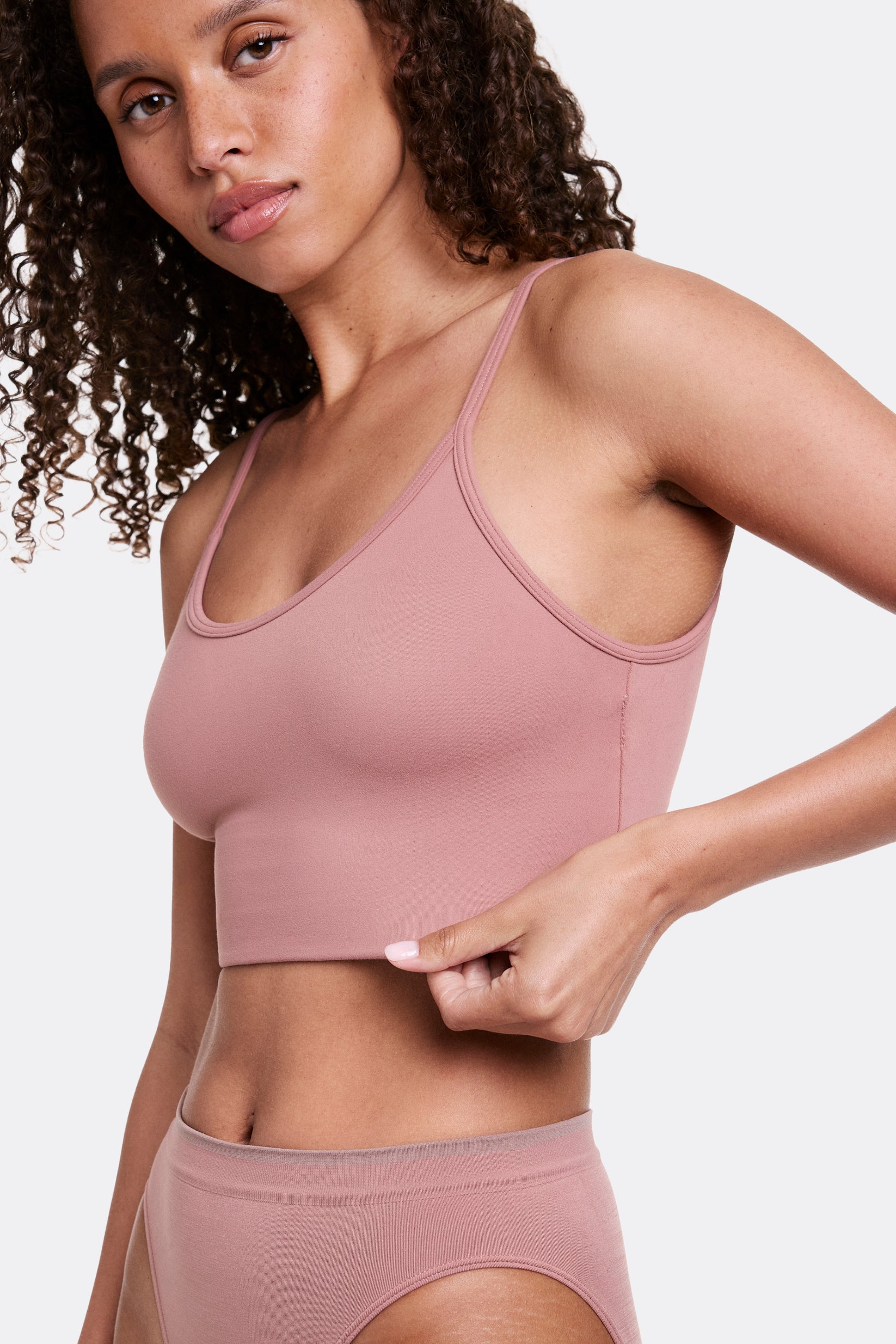 In a studio setting, Courtney wears the Whipped Knit Scoop Bralette in Plum, shown in a side profile while gently pulling the band. The scoop neckline and thin adjustable straps pair with soft, stretchy fabric for lightweight, wireless comfort and a smooth, longline fit. sizing: Courtney wears size Small