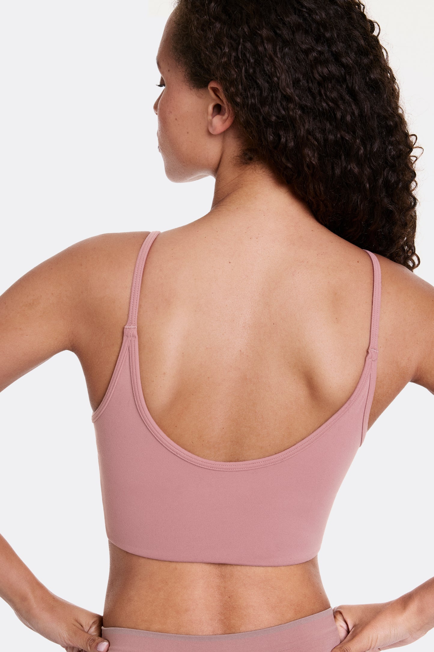 In a studio setting, Courtney wears the Whipped Knit Scoop Bralette in Plum, shown from the back with a scoop back design and thin adjustable straps. The soft, stretchy fabric provides lightweight, wireless comfort with a smooth, longline fit.