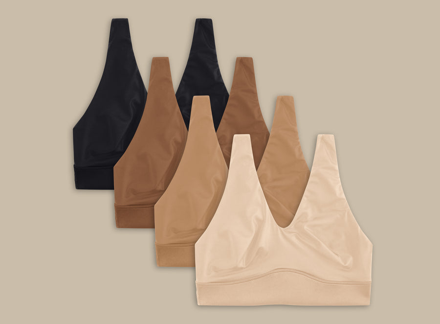 Flat lay of four Bliss Bralettes in various colors against a dark cream background. From left to right - Black, Brown, Tan and Beige.
