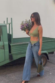 Model standing beside a vintage mint-green truck wearing the Bliss Plunge Bralette in Dill, holding wildflowers, styled with wide-leg jeans and sunglasses.