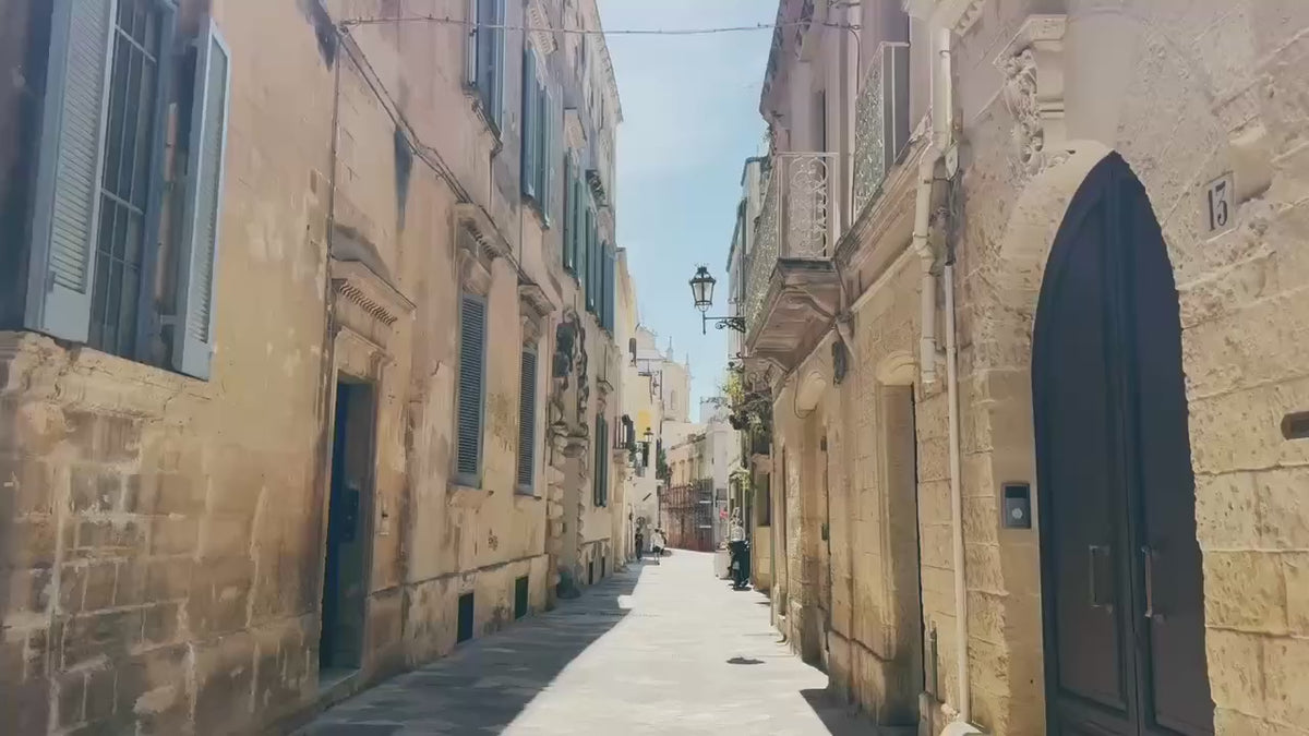 A sun-drenched cobblestone alley lined with ornate stone buildings in an Italian hill town.