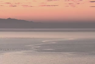 A pastel sunset over calm Mediterranean waters with a mountain silhouette on the horizon