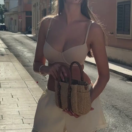 Model strolling a sun-drenched Italian street wearing the Base Balconette Bra in Beige, paired with white shorts and a woven straw bag.