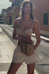 Model strolling a sun-drenched Italian street wearing the Base Balconette Bra in Beige, paired with white shorts and a woven straw bag.