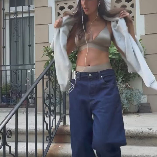 Lifestyle video of model wearing the Stretch Satin Triangle Bralette in Sable — a sleek triangle bralette in lustrous stretch satin fabric with thin adjustable straps — paired with the Stretch Satin Highwaist Thong in Sable, paired with Jeans and a sweatshirt.