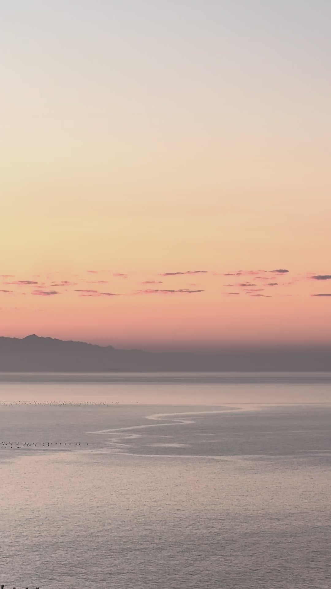 A pastel sunset over calm Mediterranean waters with a mountain silhouette on the horizon