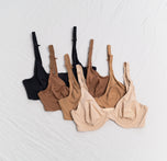 Flatlay of four Base Unlined Bras in the colors Black, Brown, Tan and Beige