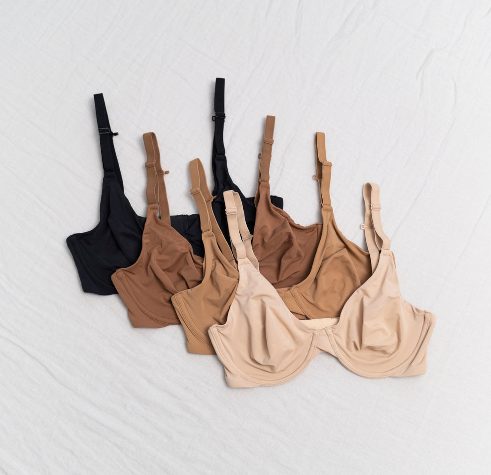 Flatlay of four Base Unlined Bras in the colors Black, Brown, Tan and Beige